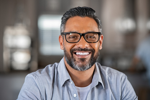 Smiling mature indian man wearing spectacles and looking at camera. Portrait of middle eastern confident businessman at office. Portrait of successful mid entrepreneur feeling satisfied and working from home.